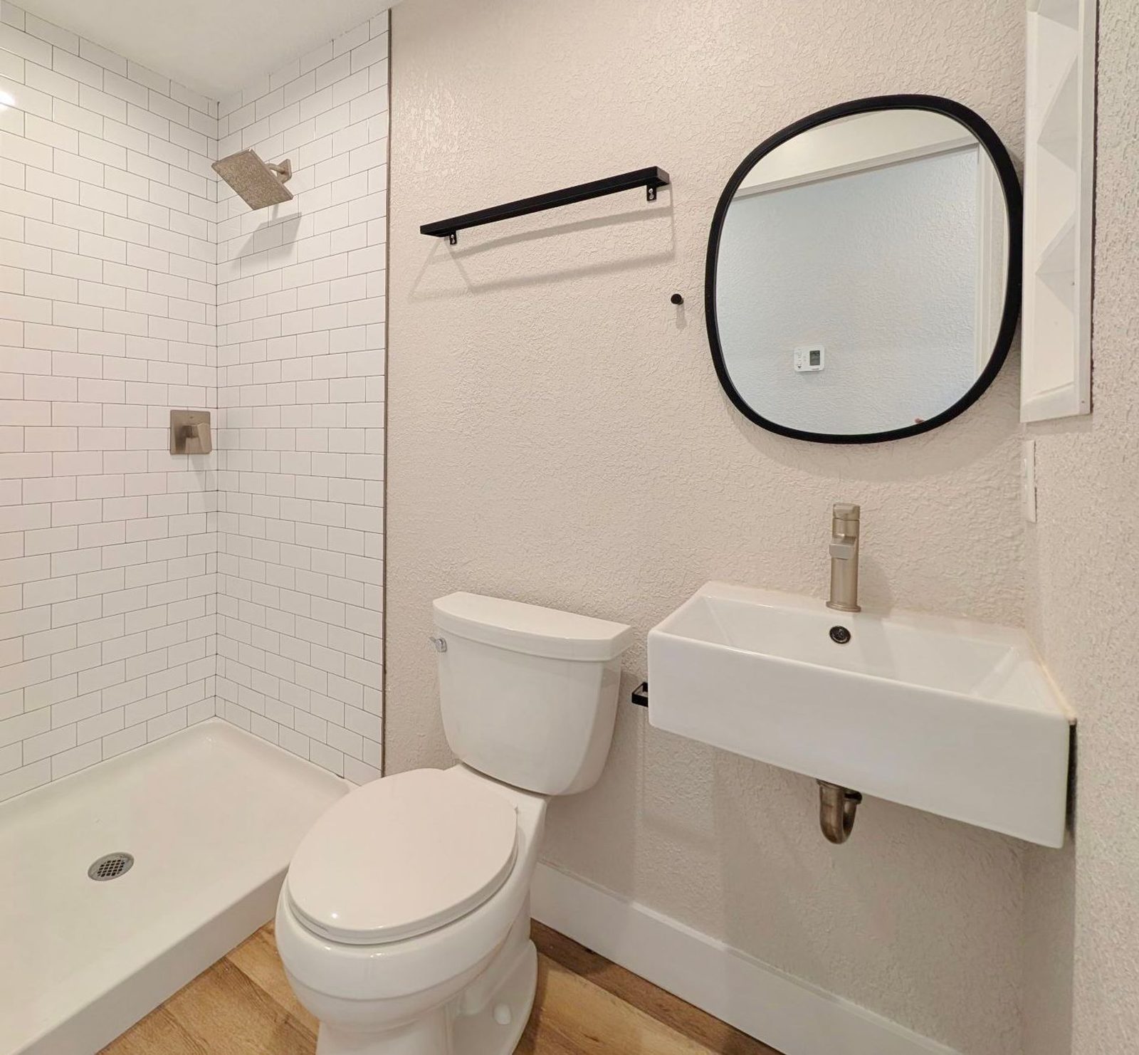 Bathroom with white tile walk-in shower and round mirror at Ashley Lofts